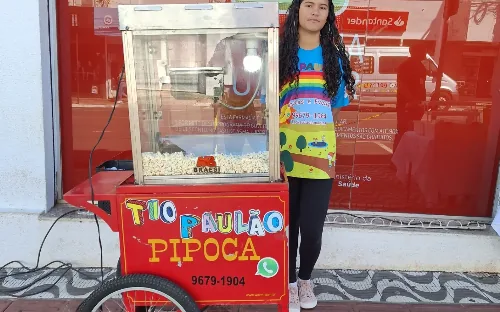 Carrinho vermelho de pipoca com o nome Tio Paulão Pipoca na porta de uma loja