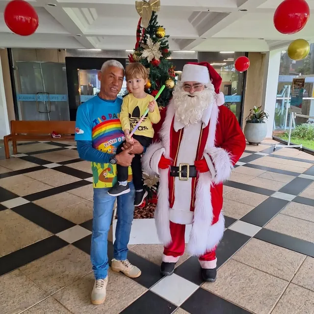 Papai Noel com o Tio Paulão e uma criança diante da árvore de Natal