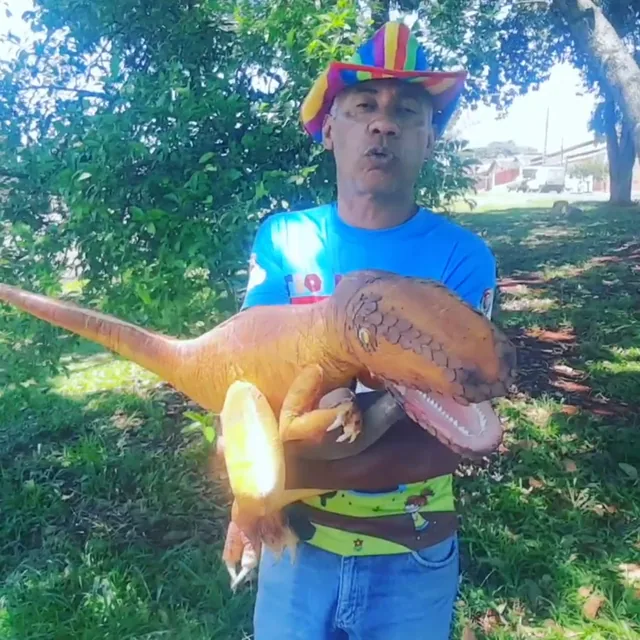 Tio Paulão de chapéu colorido segurando um filhote de dinossauro